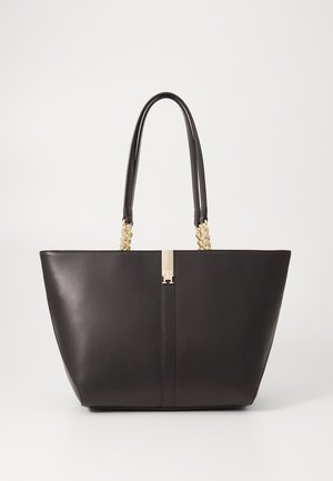 Zwarte leren tote bag met dubbele handvatten met gouden kettingen en een centrale gouden gesp op een effen achtergrond.