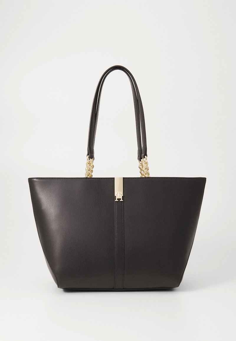 Sac cabas en cuir noir avec double poignée comprenant des chaînes dorées et un fermoir central doré sur un fond uni.