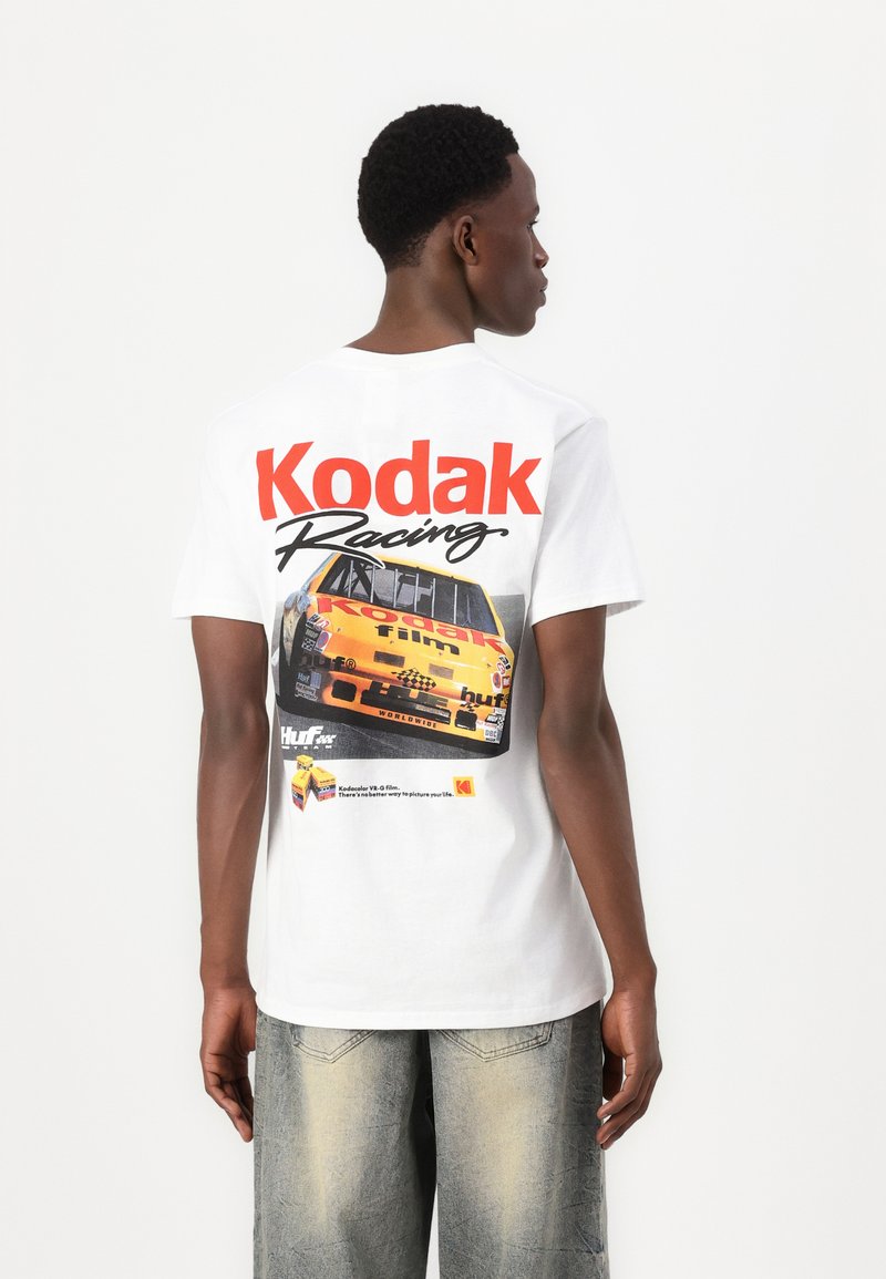 Bílý bavlněný tričko s nápisem "Kodak Racing" v červeném písmu, s grafikou žlutého závodního auta a logo akcenty na zadní straně.