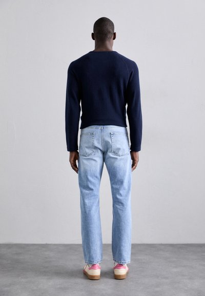 Marineblå strikkegenser, lyseblå denimjeans og sko med rosa detaljer. Ovn består av en tettsittende design med en uformell, avslappet passform.
