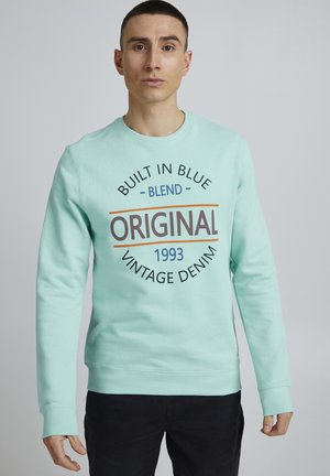 Mintgroene sweatshirt met een ronde hals, geribbelde manchetten en een grote grafische print met "BUILT IN BLUE," "ORIGINAL," en "VINTAGE DENIM 1993."