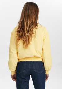 Gul sweatshirt med puffärmar och ribbat fåll, matchad med mörkblå jeans. Slät textur och avslappnad passform.