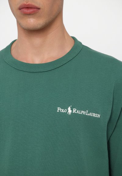 Zaļš kokvilnas T-krekls ar apaļu izgriezumu, uz kura ir baltais izšūtais "Polo Ralph Lauren" logs un neliels zirggrafika kreisajā krūtīs.