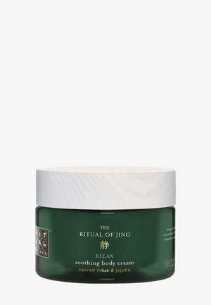 Bocal en verre vert avec un couvercle en bois blanc. L’étiquette comporte un texte doré indiquant "Le Rituel de Jing", "Détente", et "crème corporelle apaisante."
