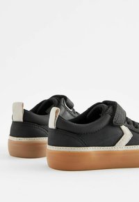 Svarta sneakers med ovandel i canvas, gummisula och beige accenter. Har ett kardborreband och sydda detaljer på sidan.