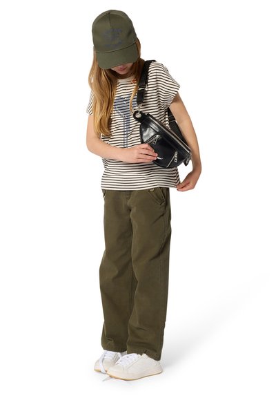 T-shirt rayé avec un motif graphique, pantalon vert olive, sac bandoulière noir avec des zips, et baskets blanches. Casquette olive avec texte.