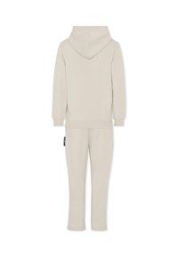 Tuta con cappuccio color beige chiaro, caratterizzato da una morbida texture del tessuto, polsini a coste e un'etichetta sui pantaloni. Progettato per un fit rilassato e comfort.