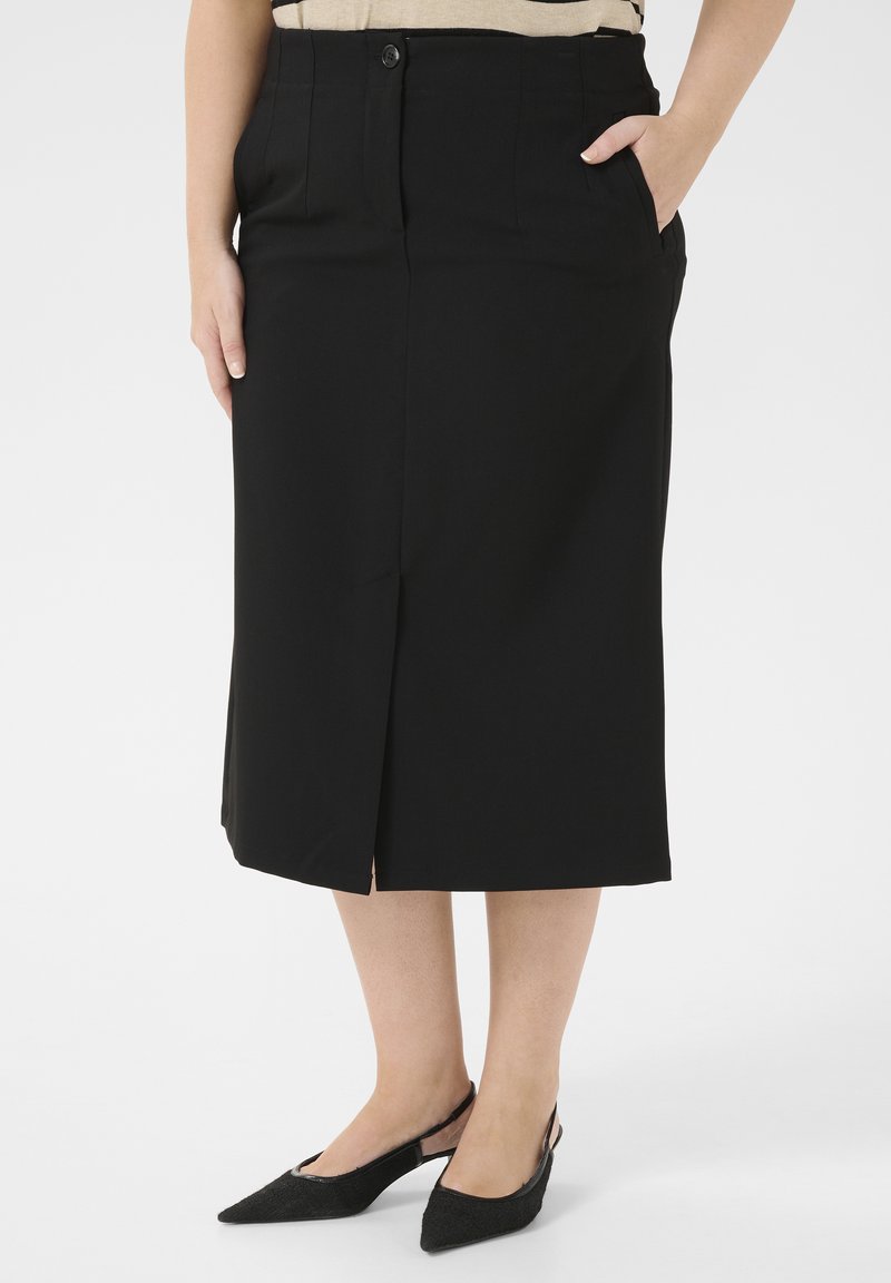 Zwarte kokerrok met een aansluitende taille, knoopsluiting aan de voorkant, zijzakken en een split aan de zoom. Gemaakt in combinatie met zwarte slingback schoenen.