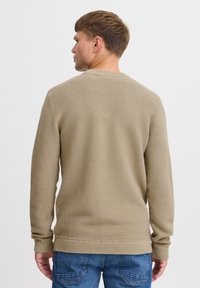 Khaki geribd sweater met lange mouwen, ronde hals en textiel stof, gecombineerd met blauwe denim jeans. Weergave van achteraf.