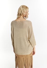 Top in maglia beige con scollo ampio e maniche larghe, abbinato a una gonna in suede con frange, entrambi con una consistenza morbida.