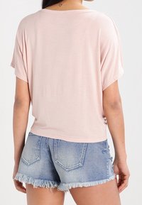 Ljusrosa kortärmad skjorta med lös passform, tillsammans med högmidjade denimshorts med fransade kanter och en klassisk femfickdesign.