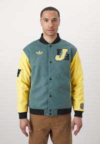 Fleece varsity jacket with teal body, yellow sleeves, black collar, and buttons. Features embroidered logo and patches on front and sleeve.