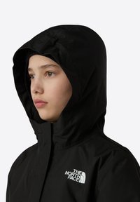 Veste à capuche noire en tissu lisse, dotée d'une fermeture éclair et d'un logo blanc bien en vue sur la poitrine.