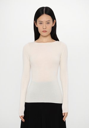 Haut long à manches beige clair en matériau tricot fin et doux. Doté d'un col large et arrondi et d'une silhouette cintrée.