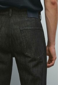 Dunkelblaue Jeans mit strukturiertem Finish, ausgestattet mit zwei Gesäßtaschen und einem Lederlabel am Bund, seitlich dargestellt.