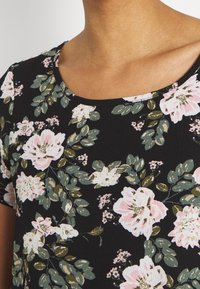 Blommig svart t-shirt med rund halsringning, korta ärmar och en texturerad tyg. Designen inkluderar rosa och vita blommor med gröna blad.