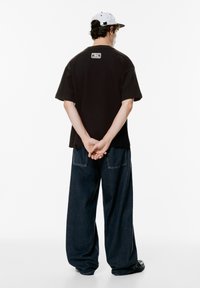 Sort kortærmet t-shirt med ryg-logo, kombineret med løse mørke denimjeans. Kappen er hvid med en sort skygge og har snapback lukning.