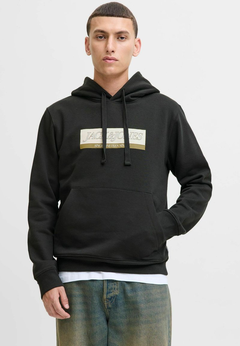 Sort hættejakke med en frontlommekanaguru, prydet med et hvidt og guld logo grafik, ribbede ærmer og kant, båret over en hvid t-shirt.