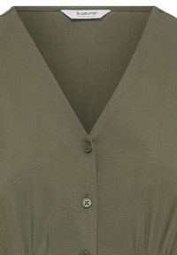 Blouse vert olive à col en V avec trois boutons sur le devant et une étiquette portant l'inscription "b.young the collection" à l'intérieur de l'encolure.