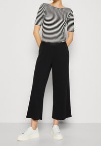 Czarne spodnie o szerokich nogawkach połączone z czarno-białą, paskowaną bluzką z krótkim rękawem. Stylizacja wyróżnia się prostym fasonem i casualowymi, białymi trampkami.