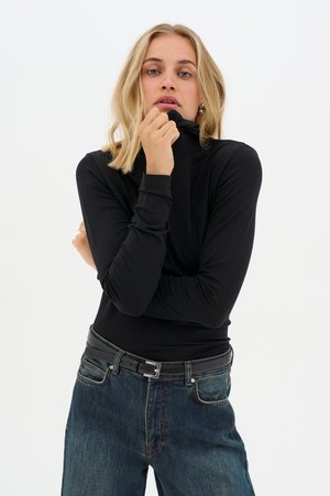 Black long-sleeve turtleneck shirt with fitted design and soft texture, paired with high-waisted blue jeans and a black belt.