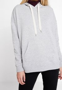 Sudadera con capucha color gris claro hecha de una suave mezcla de algodón, con bolsillo tipo canguro en el frente, cordones blancos ajustables y puños y dobladillo acanalados.
