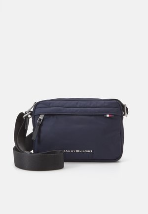 Donkerblauwe crossbodytas met zwarte verstelbare band, voorvak met ritssluiting en klein Tommy Hilfiger-logo aan de voorkant.