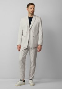 Hellegraue, doppelt geknöpfte Blazerjacke mit braunen Knöpfen, passende maßgeschneiderte Hose und weiße Sneakers. Der Stoff hat eine dezente Textur.