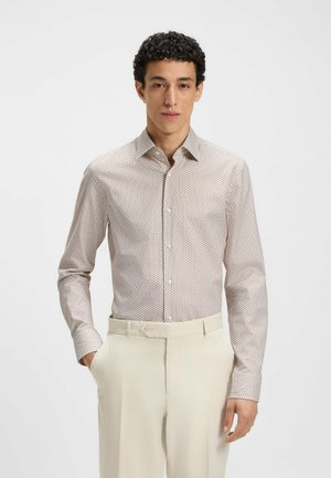 Langärmliges, hellbeiges Hemd mit kleinem Druckmuster, Knopfverschluss und Kragen. Zusammen mit cremefarbenen Hosen für einen neutralen Look getragen.