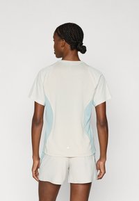 Αθλητικό τοπ σε ανοιχτό γαλάζιο και αχνό γκρι με κοντά μανίκια, διαθέτει υφή από δίχτυ και λεπτομέρειες σε πλαϊνές πινελιές. Συνδυάζεται με ανοιχτόχρωμα σορτς.