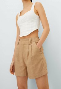 Vitt kort topp med en strukturerad design och lätt ribbing, som är matchad med beige höga shorts som har en framfåll och sidfickor.