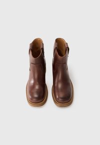 Braune Leder-Stiefeletten mit runder Spitze, seitlichen Ausschnitten und strukturiertem Sohlenprofil. Verfügt über genähte Details und eine glatte Oberfläche.