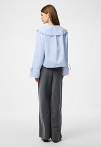 Ανοιχτό μπλε πουκάμισο με ρίγες, μεγάλο περίγραμμα γιακά και φουσκωτά μανίκια. Συνδυάζεται με γκρι παντελόνι ψηλής μέσης και φαρδιάς γραμμής.