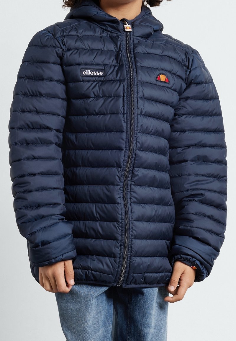 Marinblå puffjacka med quiltat mönster, med dragkedjestängning och huva. Varumärkeslogotyp på bröstet och distinkt accentdetaljering.