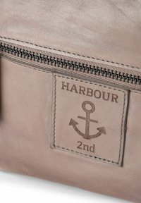 Borsa in pelle grigia con cerniera, caratterizzata da un'ancora in rilievo e dal marchio "HARBOUR 2nd" su una toppa rettangolare. Texture liscia.