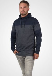 Felpa con cappuccio in blu navy e grigio mélange, caratterizzata da un corpo testurizzato, maniche a contrasto e cordini intrecciati. Vestibilità slim con un branding discreto.