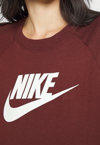 Burgundyröd sweatshirt med en vit Nike-logotyp; har rund halsringning och raglanärmar; mjukt, texturerat tyg.