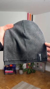 Grijze gebreide muts met een zachte textuur, effen kleur en een geribbelde rand. Heeft een klein zwart label aan de zijkant.