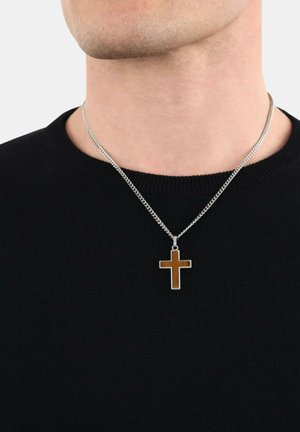 Silberne Kettenhalskette mit einem rechteckigen braunen Holz-Kreuzanhänger, getragen über einem schwarzen gerippten Pullover.