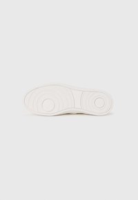 Semelle de sneaker blanche avec un design texturé, présentant des motifs circulaires et des stries pour l'adhérence. Surface lisse avec un léger brillant.