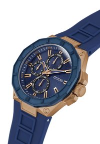 Reloj azul marino con caja octagonal dorada, tres subesferas y correa de goma. Presenta detalles en dorado y un bisel azul texturizado.