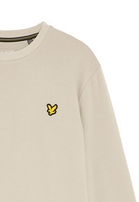 Camicia a maniche lunghe beige chiaro con scollatura tonda. Presenta un piccolo logo di un uccello ricamato giallo sul lato sinistro del petto. Texture liscia.