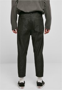 Dunkelgraue Jeans mit schmalem Schnitt, fünf Taschen und dezenten Nähten. Getragen mit schwarzen Schuhen und weißen Socken.