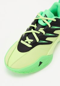 Chaussure de sport avec un dessus vert citron, accents noirs, maillage texturé et matériaux synthétiques, dotée d'une semelle verte avec un motif en chevrons.