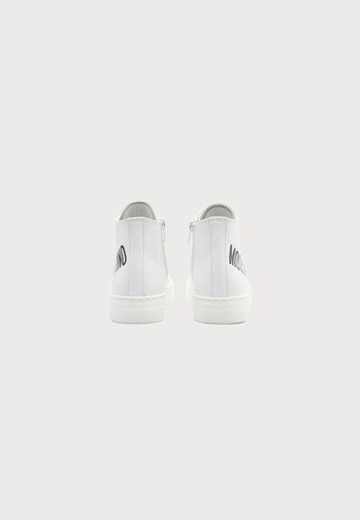 Paire de baskets blanches montantes vues de dos avec des fermetures éclair visibles et un texte noir partiellement visible sur chaque chaussure.