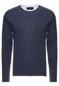 Pull-over en maille bleu marine à manches longues avec un col rond blanc, texture lisse et une petite étiquette noire sur l'ourlet inférieur. Design simple et classique.