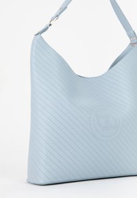 Lys blå læder skuldertaske med diagonale perforeringer, glat tekstur og et cirkulært præget logo. Justerbar rem med gyldent hardware.