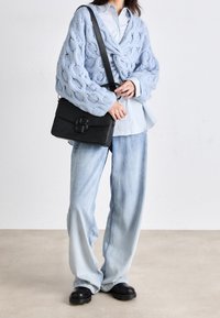 Light blue knitted cardigan with cable pattern, paired with a light blue shirt and loose light denim jeans. Black crossbody bag with logo detail.