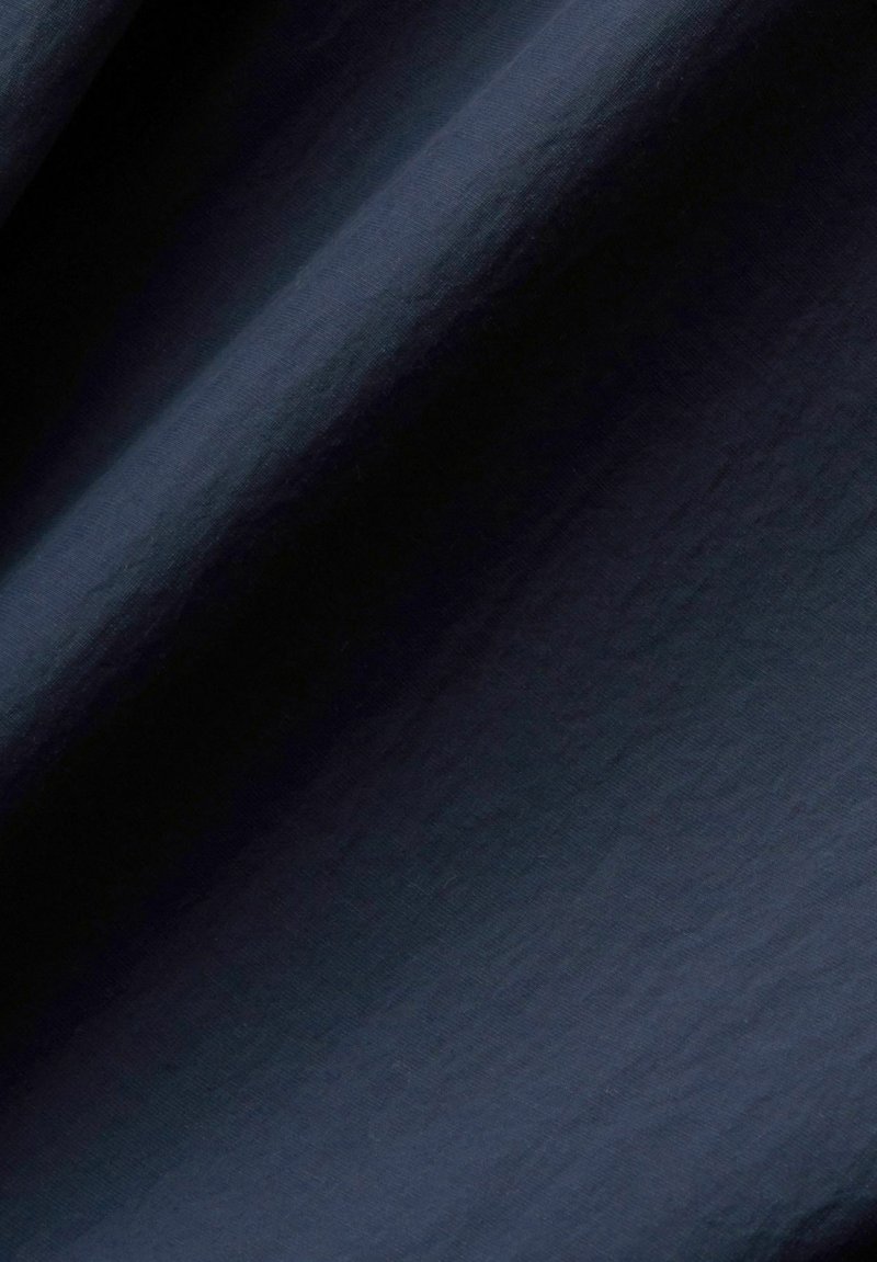 Tissu bleu marine foncé avec une texture subtile, présentant des drapés doux et fluides et un léger éclat, créant une apparence lisse et élégante.