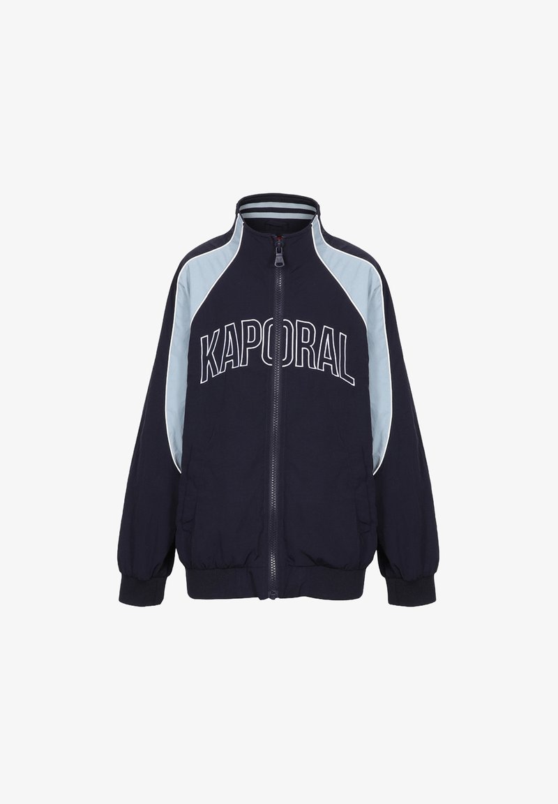 Veste zippée bleu marine avec le logo "KAPORAL" en blanc. Elle possède des empiècements d'épaule bleu clair et des poignets et un ourlet côtelés pour un look ajusté.